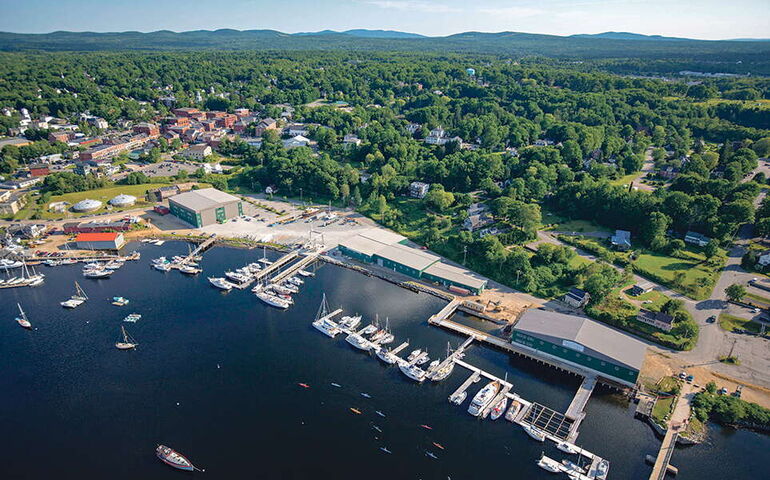An aerial view shows bulidings, boats, water and woods.