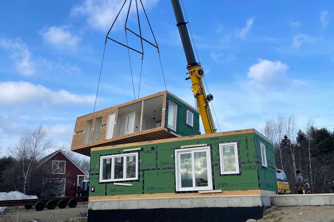 A crane lowers a wooden box onto another wooden box.