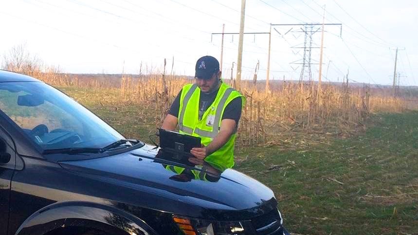 A person writes is at a computer on the hood of a car.