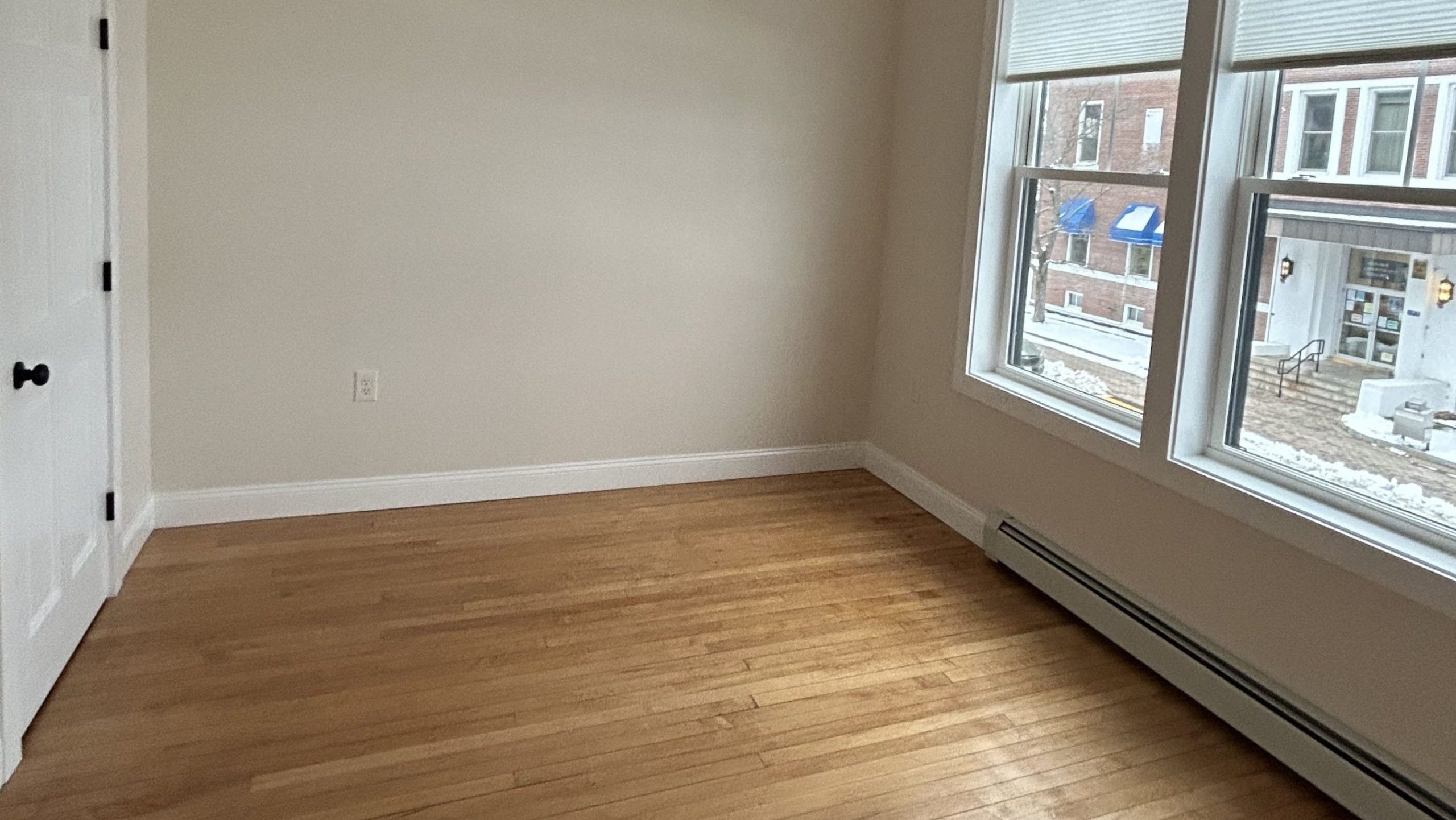 An empty room has wood floors and windows.