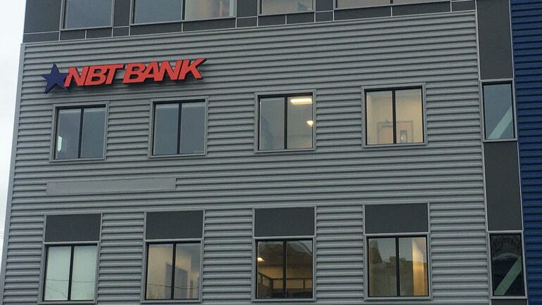 A building has dark siding and red signage.