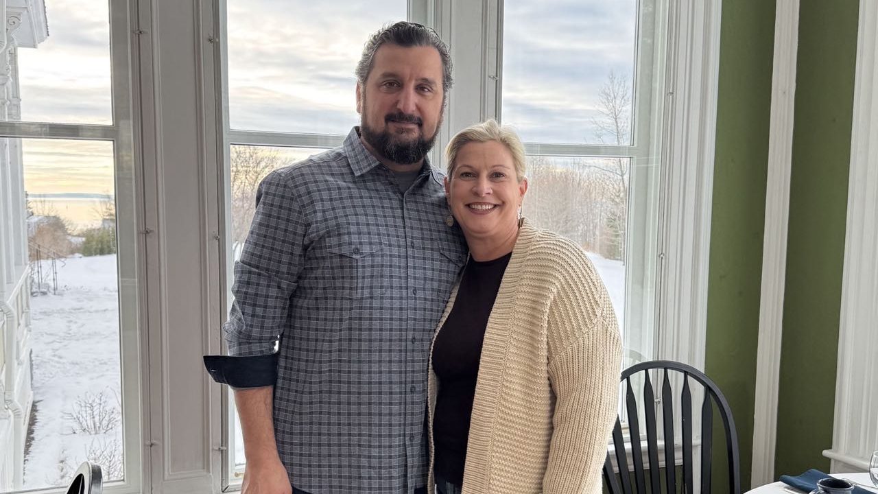 Two people pose in front of a window.