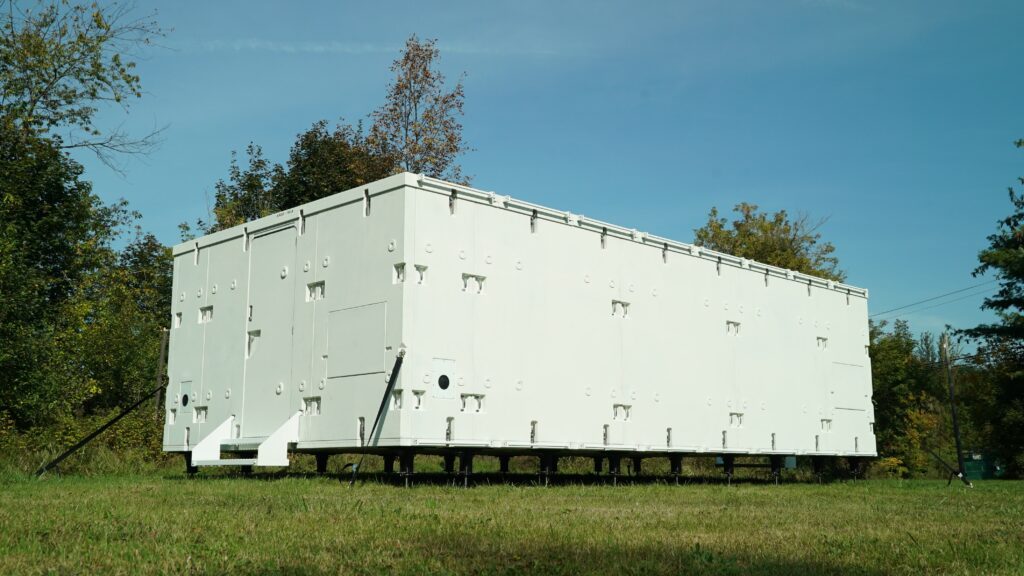 A box made with white panels sits in a field.