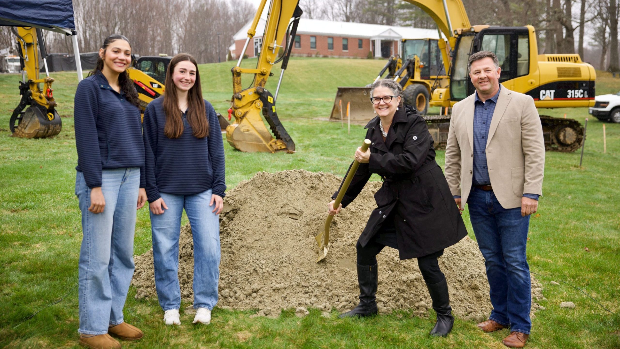 Four people pose with a mound of dirt and excavator.