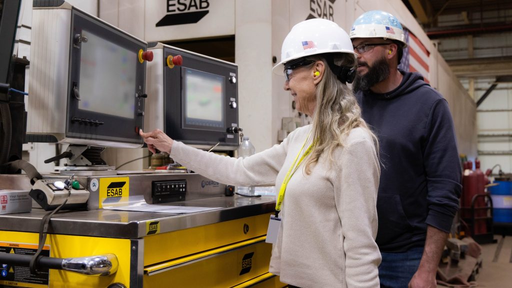 Francees Middendorf, daughter of the late J. William Middendorf, initiates the ceremonial cutting of the first steel of the Navy destroyer named for her father. She is assisted by BIW machinist Corey Bailey.