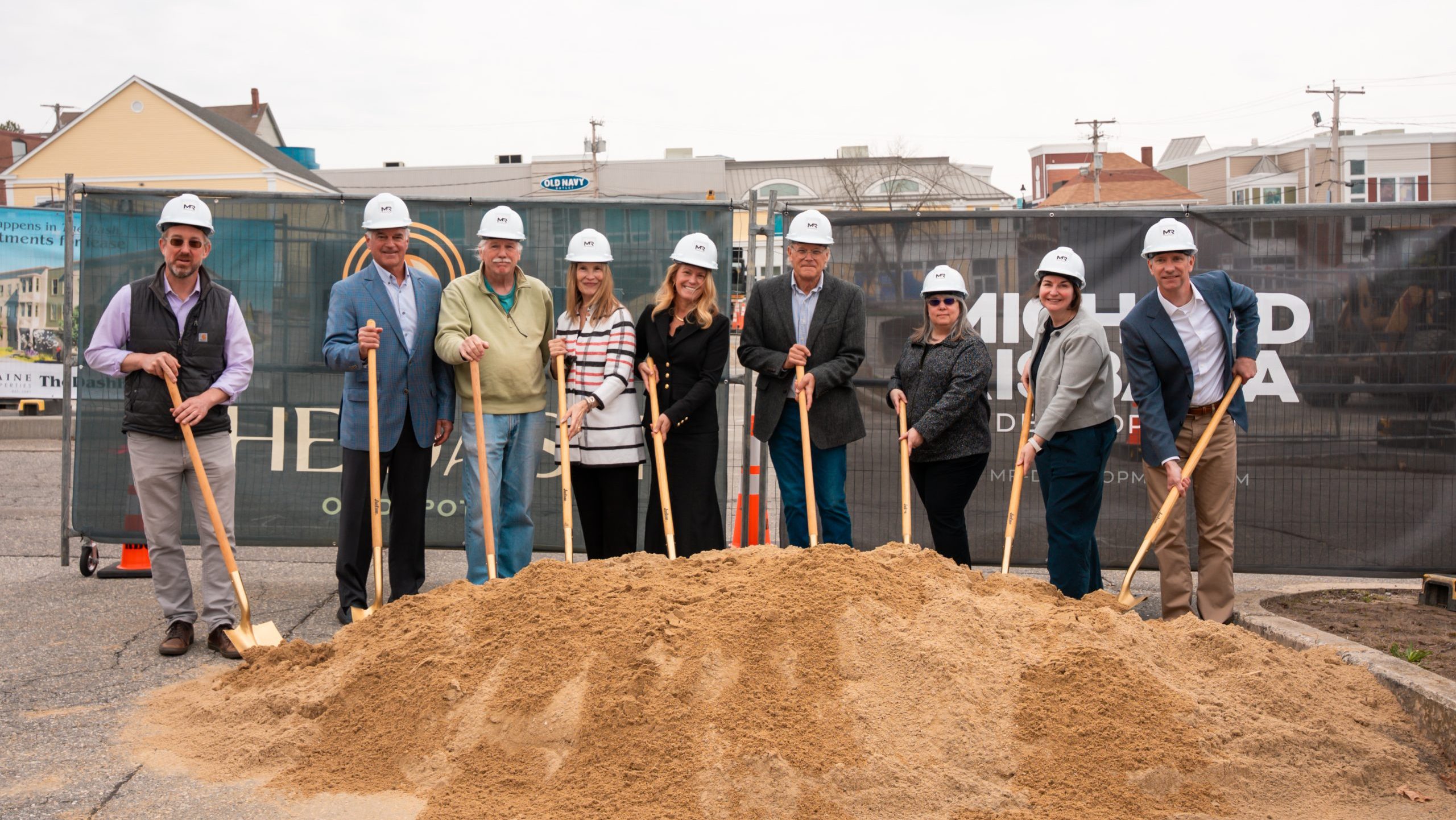 People line up at a pile of dirt with shovels.