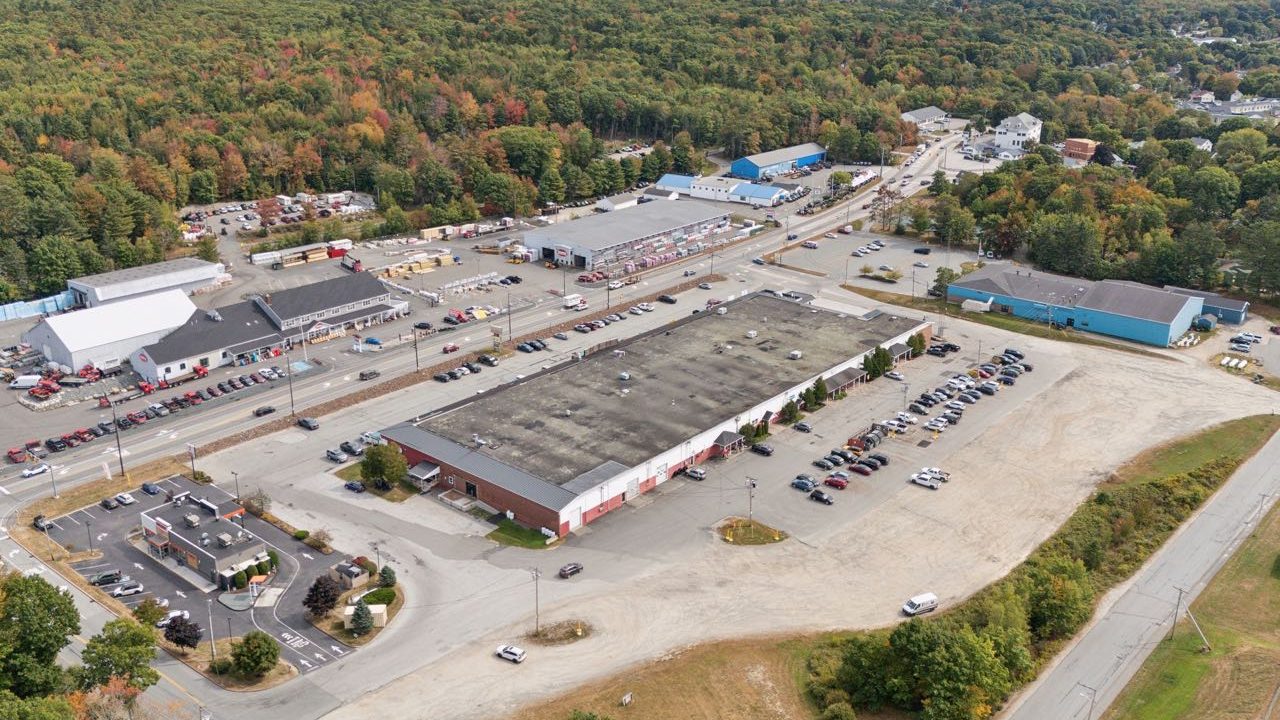 An aerial view of a large flat building surrounded by a parking lot.