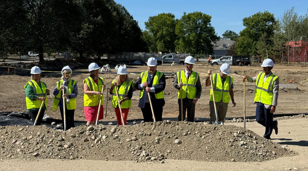 People pose in a line holding shovels and wearing hardhats.