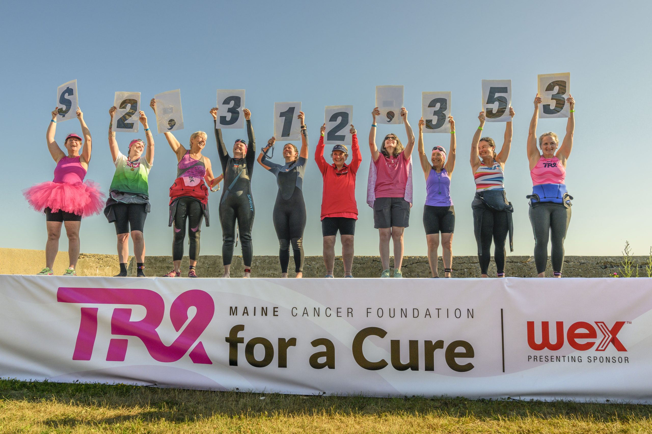 TRI ATHLETES HOLDING up signs showing funds raised 